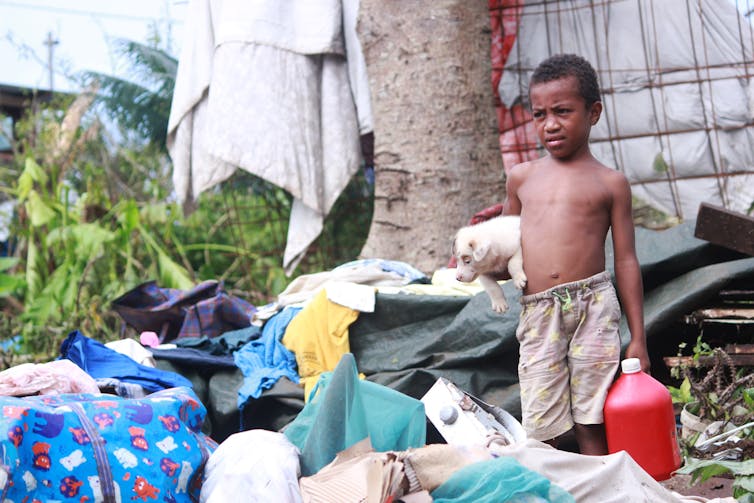 A boy holds a dog and looks at piles of rubbish