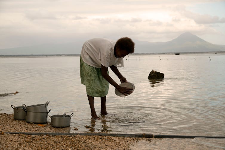 A woman washes pots in the sea