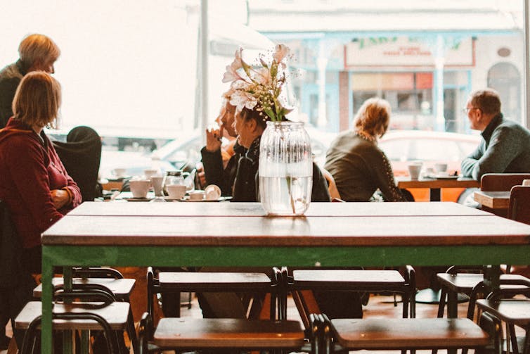 people sit at tables in a streetside cafe
