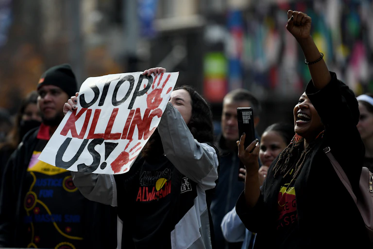 Indigenous protestors hold a sign: 'STOP KILLING US!'.