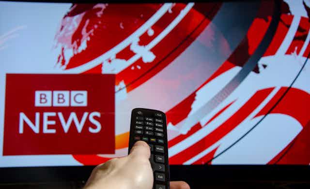 Hand points remote control at television showing BBC News broadcast