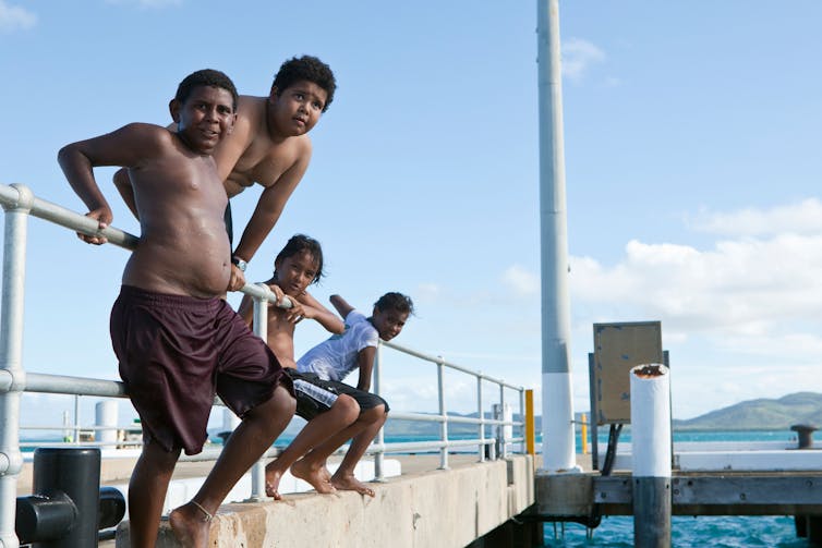 Quatro meninos descansam em um cais.