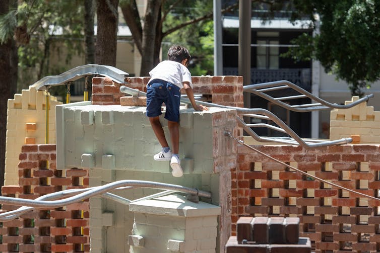A kid climbs on a brick wall.