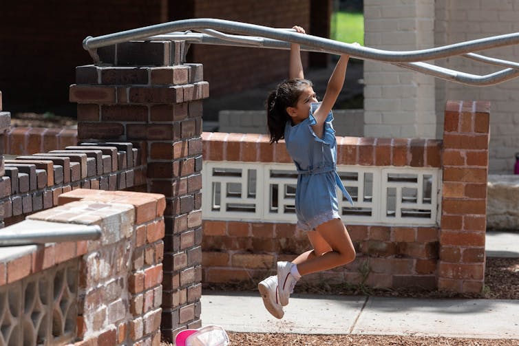 A kid swings on warped monkey bars.