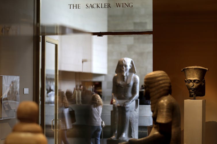 A sign reads 'The Sackler Wing' in a museum gallery exhibiting antiquities.