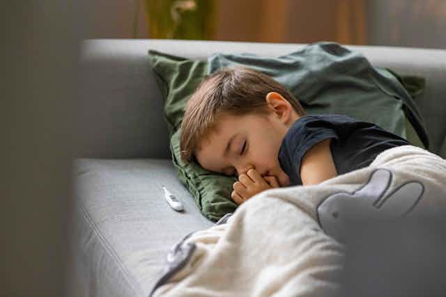 A small boy sleeps on the couch, with a thermometer in front of him.