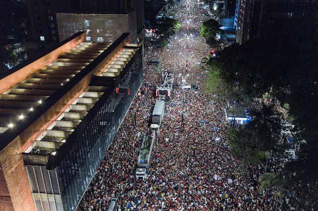 An aerial shot shows thousands of people on a city street.