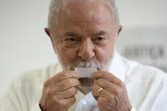 A grey-haired man kisses a piece of folded paper.