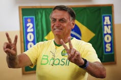 A man in yellow t-shirt with green letters that read brasilia makes the victory sign