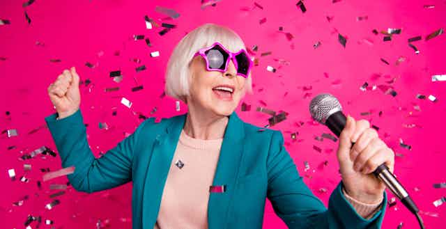 An older woman in pink star glasses holding a microphone.