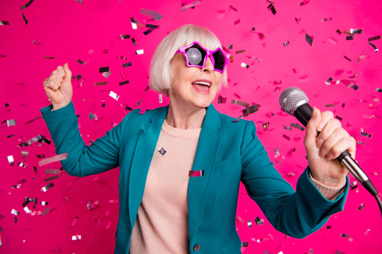 An older woman in pink star glasses holding a microphone.