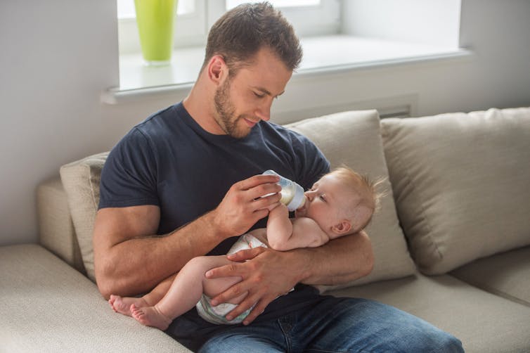 A man bottle-feeding a baby on a couch