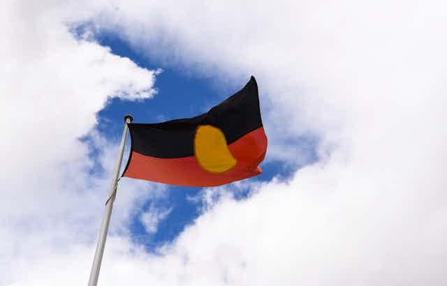 Aboriginal flag against a blue sky and clouds.
