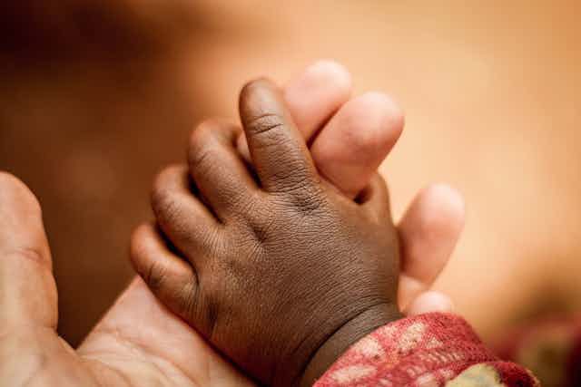 A baby's hand holding on to two fingers of an adult hand.