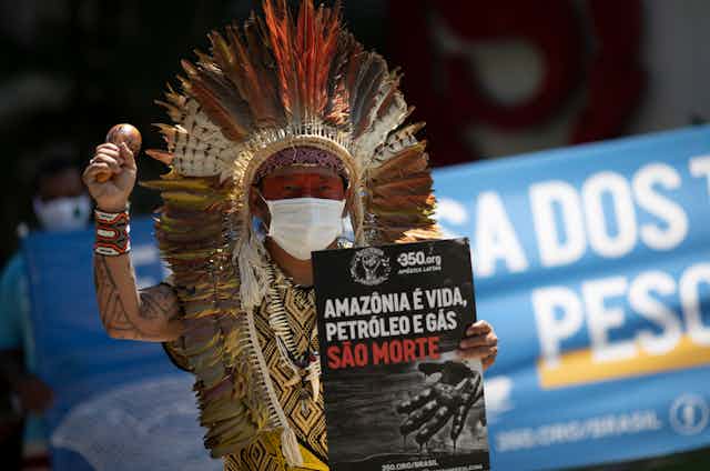 A man, Chief Ninawa, holds a sign and a music shaker. 