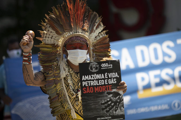 A man, Chief Ninawa, holds a sign and a music shaker.