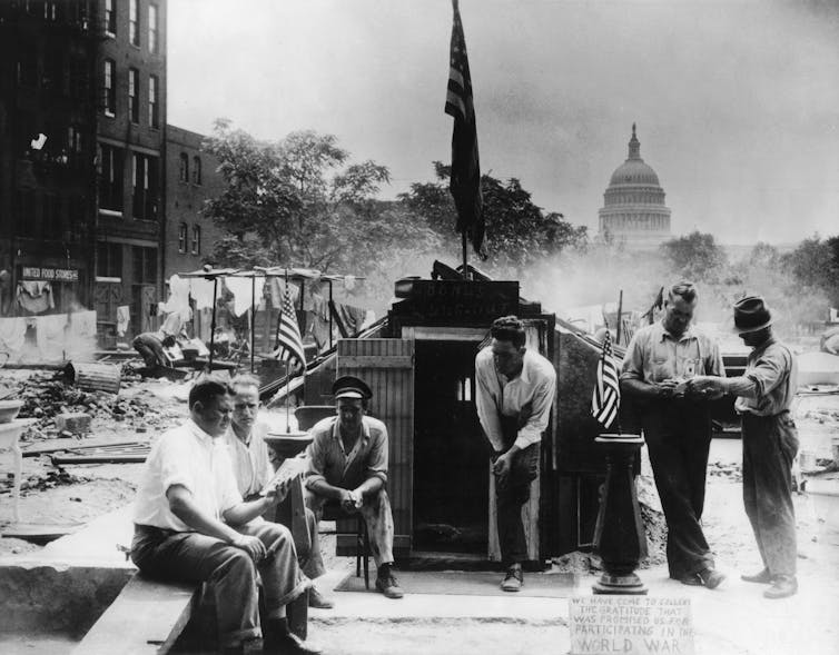 With the dome of the U.S. capitol in the background, a group of men are seated near the ruins of their camps.