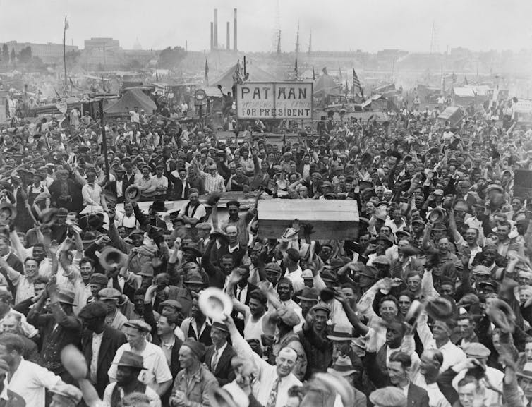 Thousands of black and white men are seen cheering with their arms waving in the air.