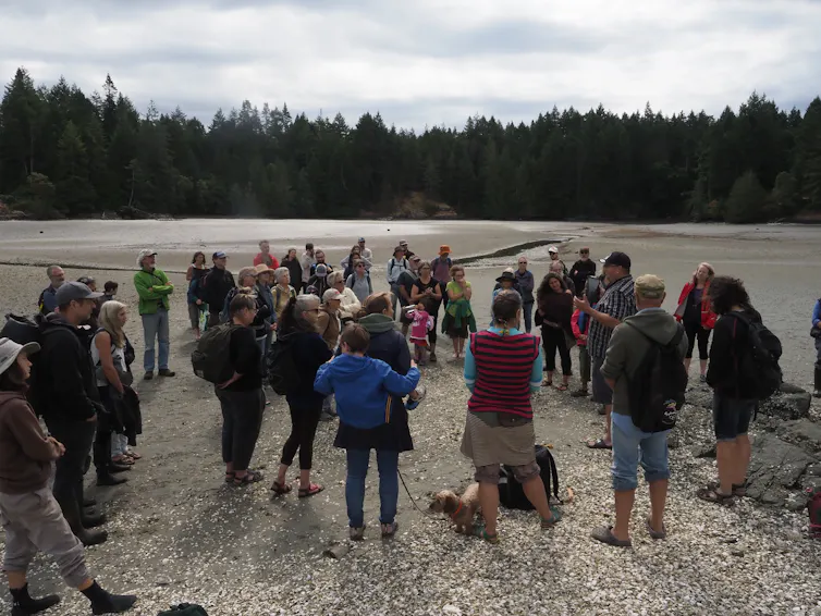 A group of people gather in a circle while a man speaks to them.