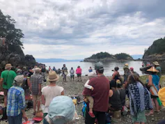 People gather in front of a shoreline. A small island can be seen in the distance.