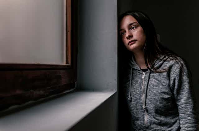 With a sad expression on her face, a teenage girl looks forlornly out the window.