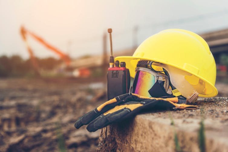 Yellow hard hat and safety goggles on a building site with cranes in the background.