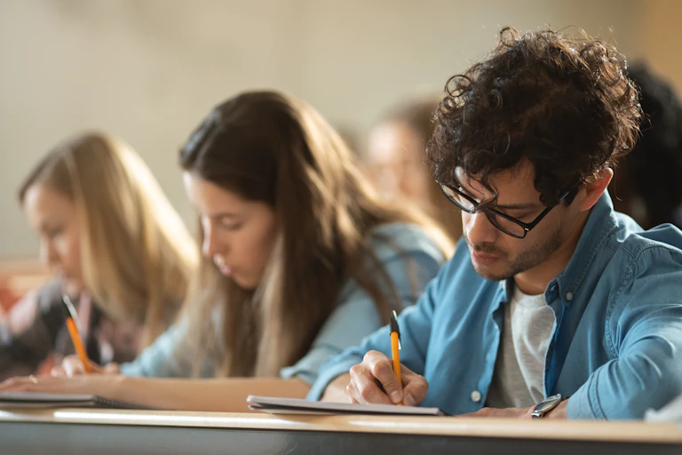 A man sits in a lecture room taking notes.