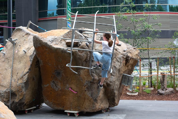 A girl climbs in a cage on a boulder.