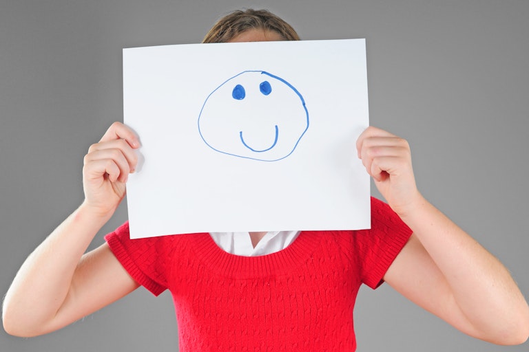 A woman holds up a smiley face mask to her head.
