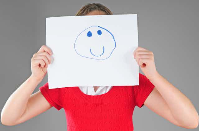 A woman holds up a smiley face mask to her head.
