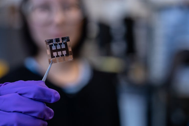 A female scientist holds a solar cell between tweezers