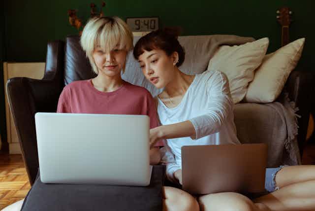 Two young women sitting on floor with laptops