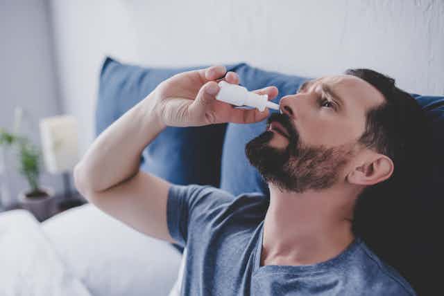 Man sitting in bed using nasal spray