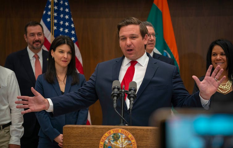 A man in a suit with a red tie at a podium.