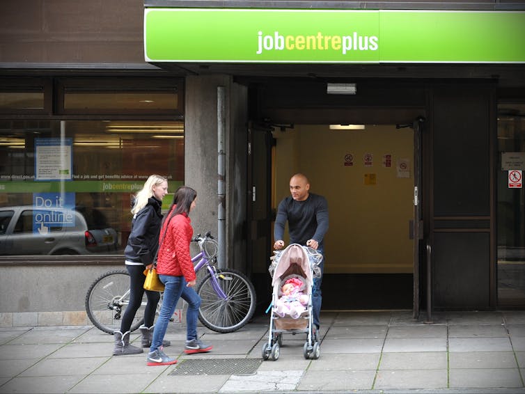 Two women with a bike and a man with a pram on a pavement.