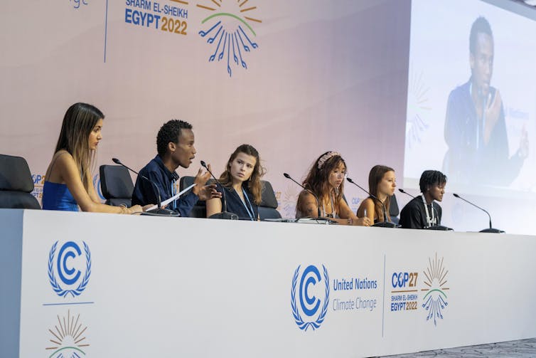 a row of six people sitting behind a table on a stage