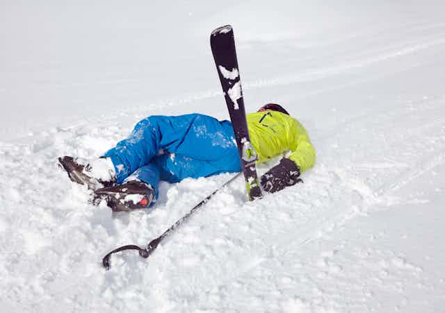 A male skier lies on his back with a ski pointing up in the air after taking a fall. 
