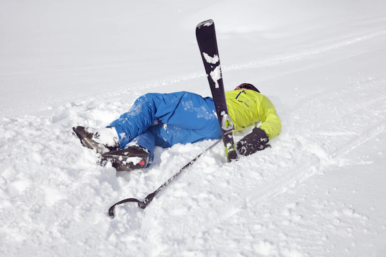 A male skier lies on his back with a ski pointing up in the air after taking a fall.