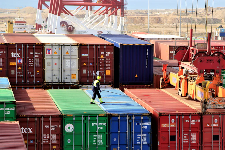 A longshoremen worked on top of pile of shipping containers