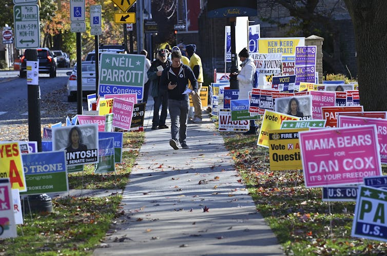 A man walks down a sidewalk that is lined with colorful campaign signs.