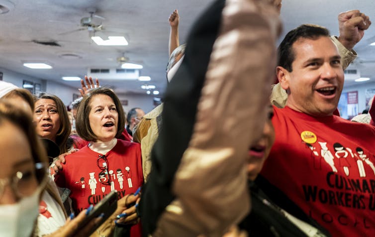 A crowd of people In red shirts raise their hands at what seems like a political rally.