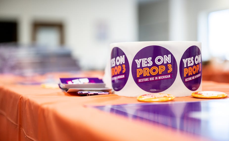 A role of stickers with 'Yes on Prop 3' written on them atop an orange table.