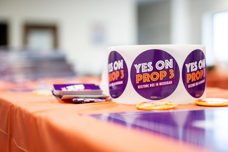 A role of stickers with 'Yes on Prop 3' written on them atop an orange table.