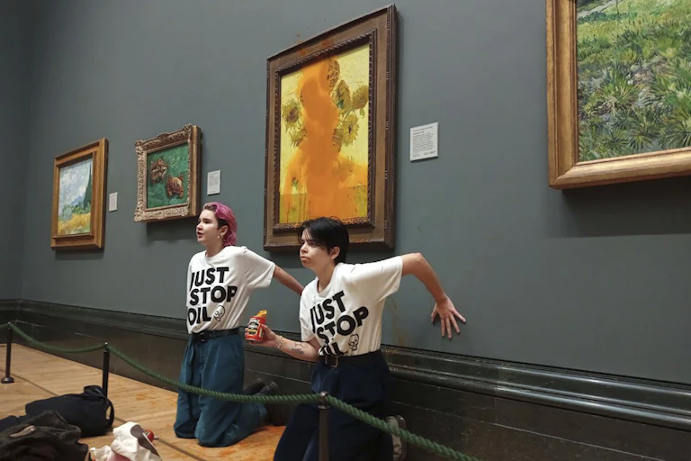 Protesters sit in front of defaced painting with hands glued to wall