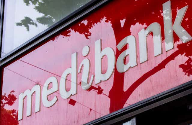White logo of medibank on a red glossy background with trees reflected on the surface