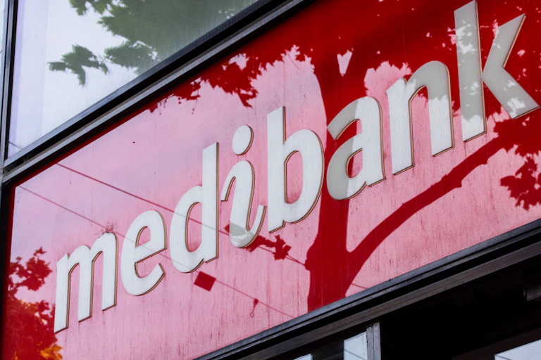 White logo of medibank on a red glossy background with trees reflected on the surface
