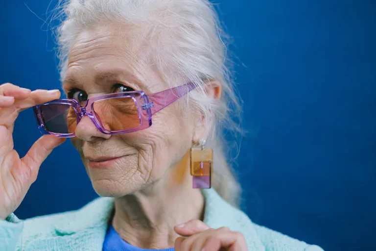 Perempuan lanjut usia melepas kacamata hitam berwarna merah muda