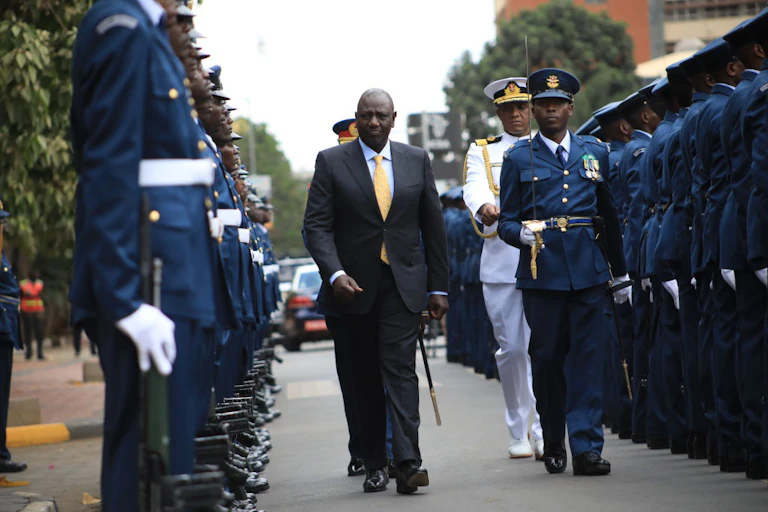 Man walking between rows of armed soldiers flanked by three senior officers.