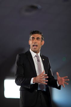 Rishi Sunak with both hands out in front of him mid-way through giving a speech.