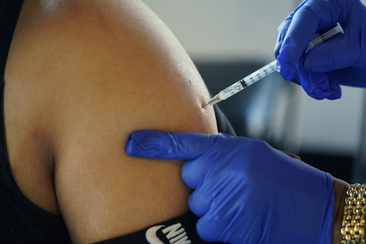 Des mains gantées faisant une injection dans une épaule